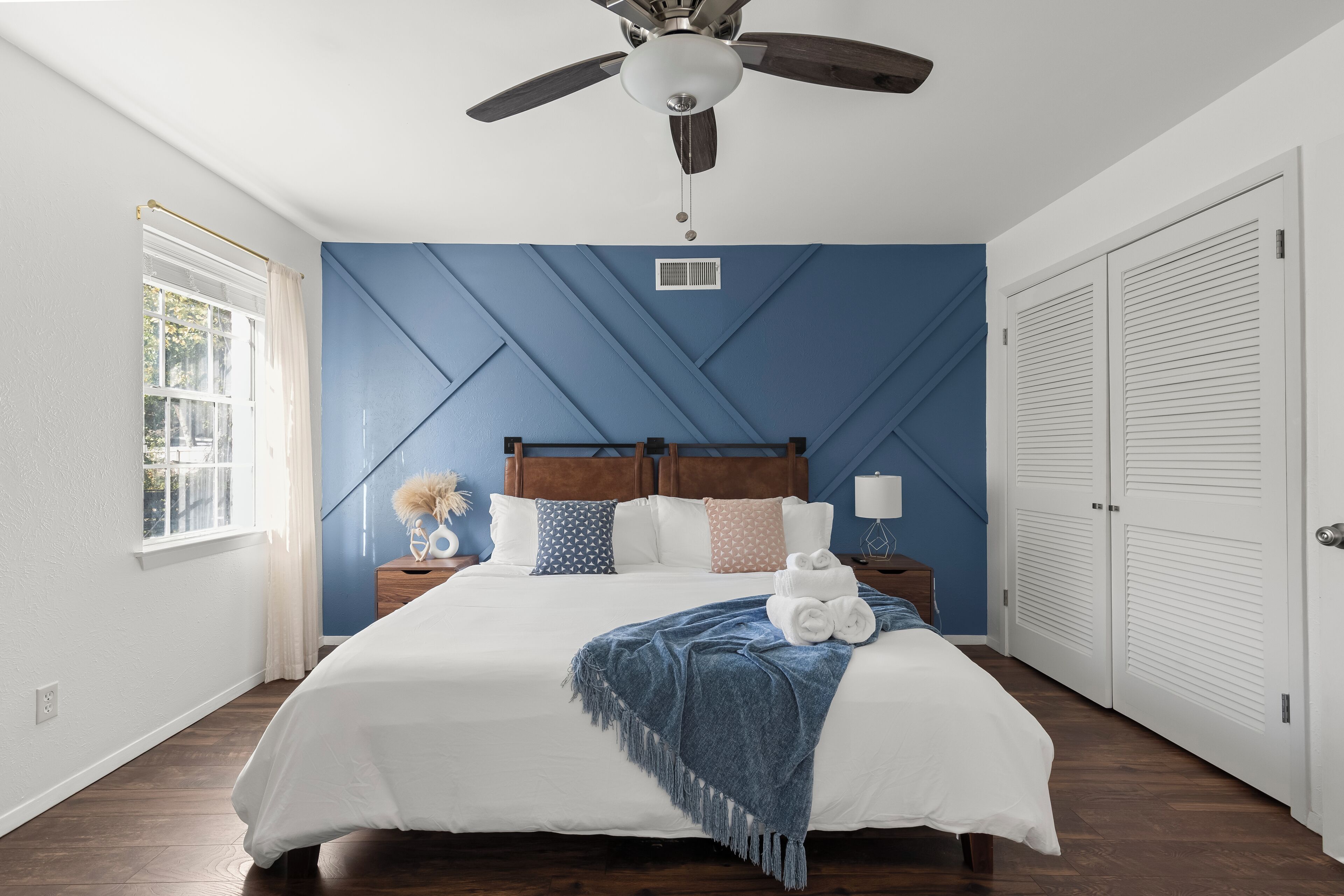 A bedroom with a bed, a ceiling fan, a window, and a door.
