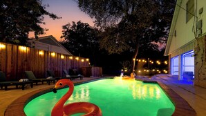 En pool med en flamingo-svømmebøje, omgivet af liggestole og lyskæder.