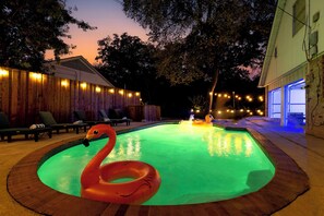 Ein Swimmingpool mit einem Flamingoboat, umgeben von Liegestühlen und Lichterketten.