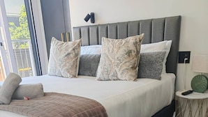 Quarto de hotel moderno com uma cama grande, cabeceira cinzenta e uma pequena mesa de cabeceira com abajur.