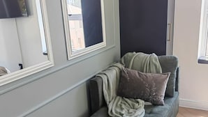 Um espaço de canto com assento acolchoado, parede escura e janela com vista para edifícios.
