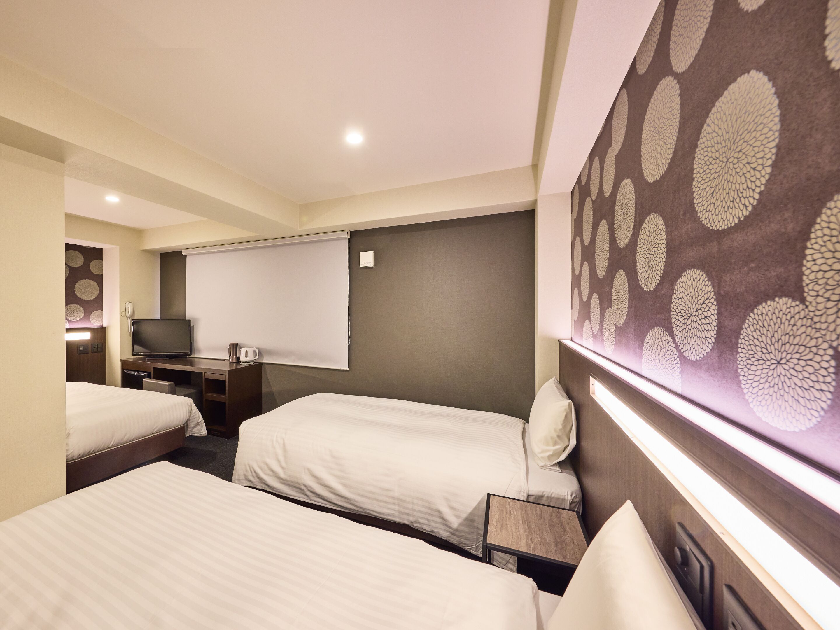 Une chambre d’hôtel avec trois lits, une télévision, un bureau avec un téléphone et un écran de projection.
