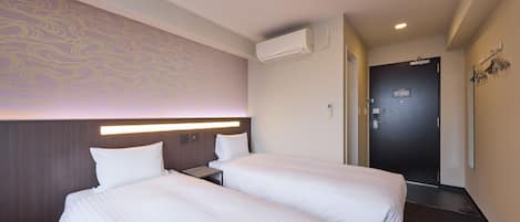 Ein Hotelzimmer mit zwei Betten, einem Kopfteil mit integrierter Beleuchtung, einer Wandklimaanlage und einer Tür mit Spiegel und Lampen.