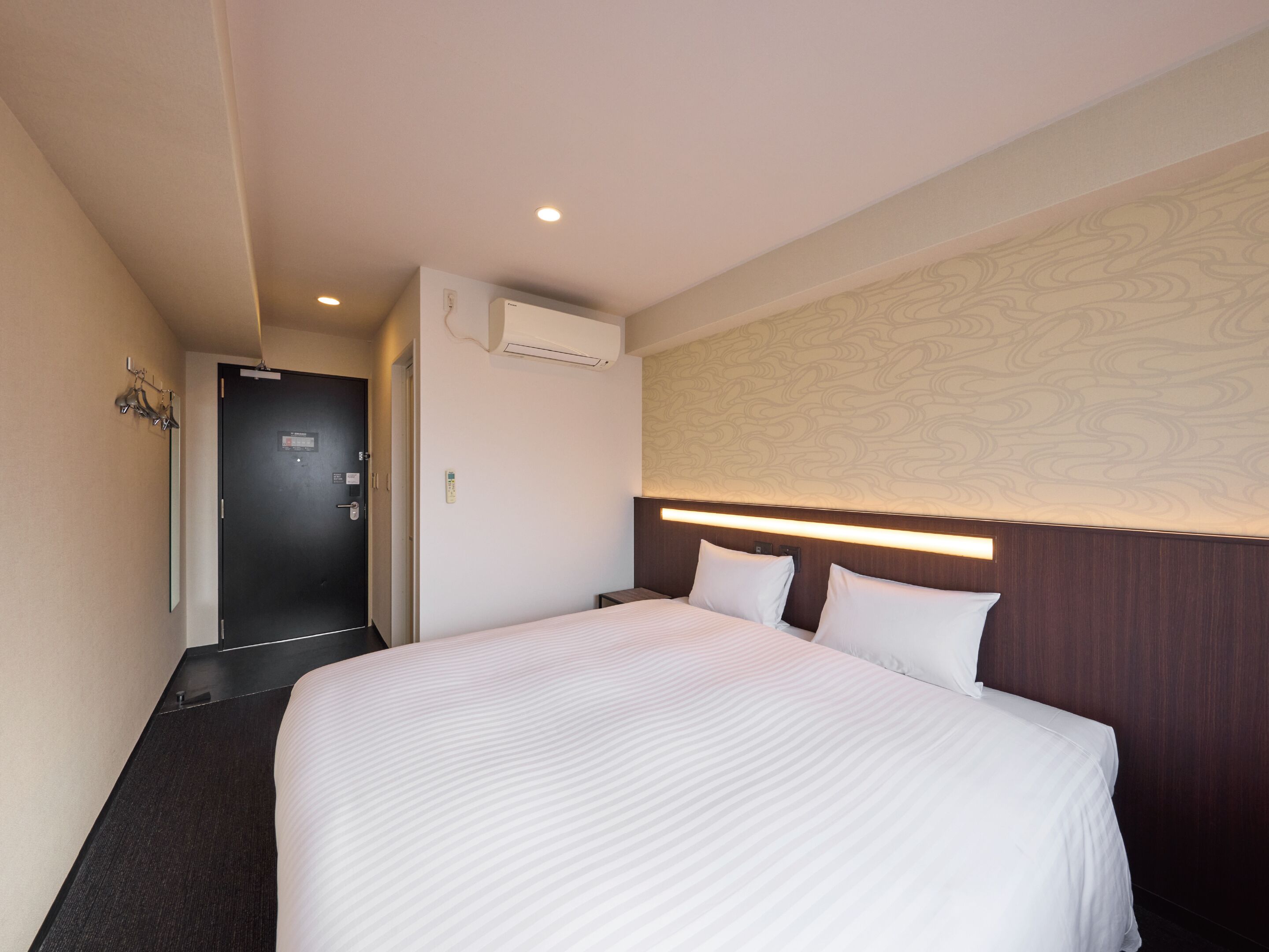A hotel room with a large bed, a dark door, an air conditioning unit, and a wall with a textured pattern.