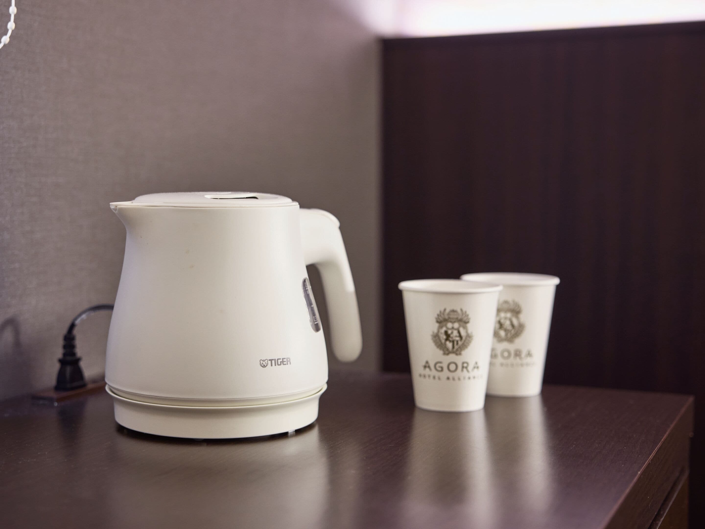 A white electric kettle and two white cups with embossed logos on a wooden surface.