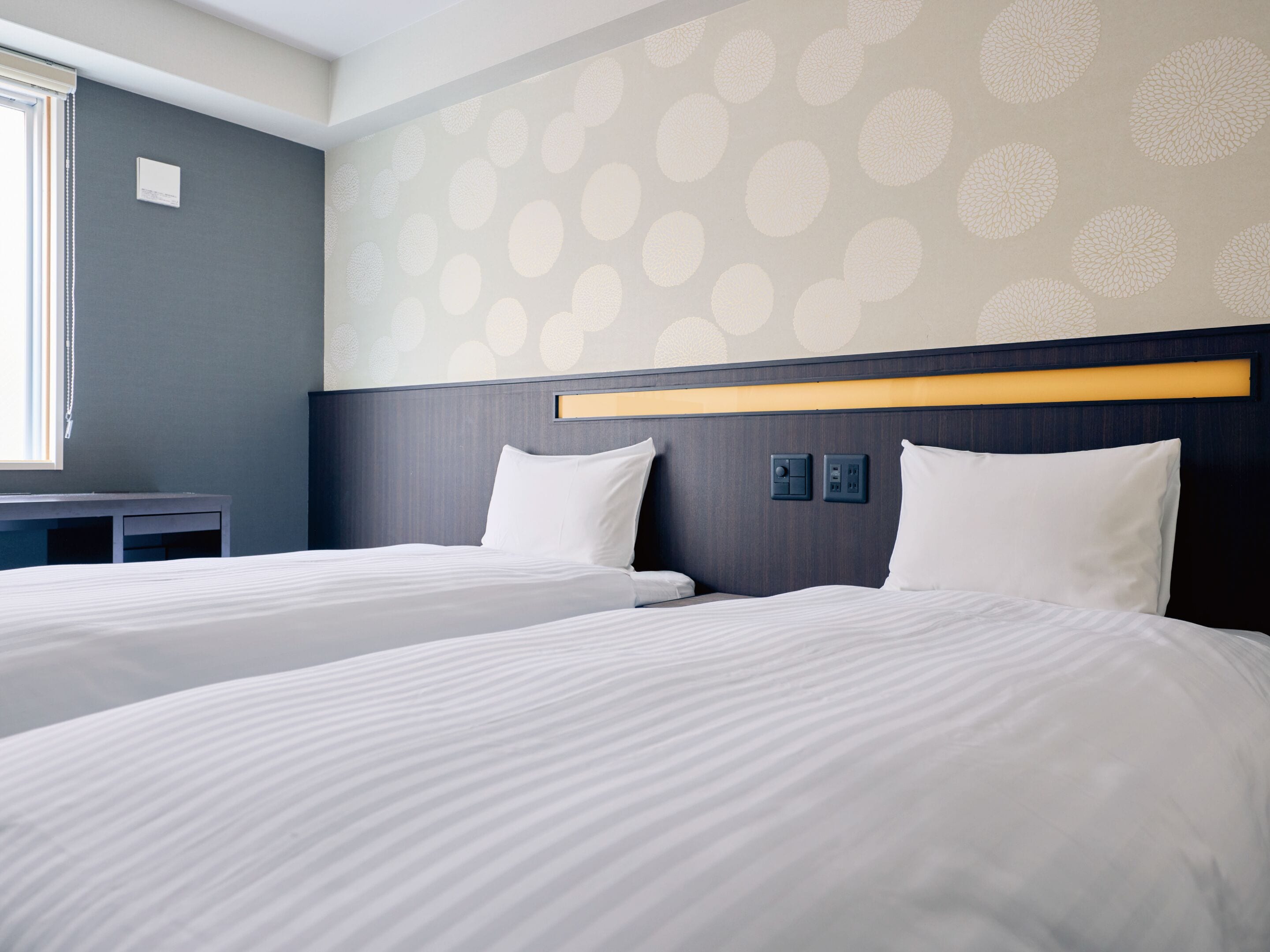 A hotel room with two beds, a desk, and a wall with circular patterns.