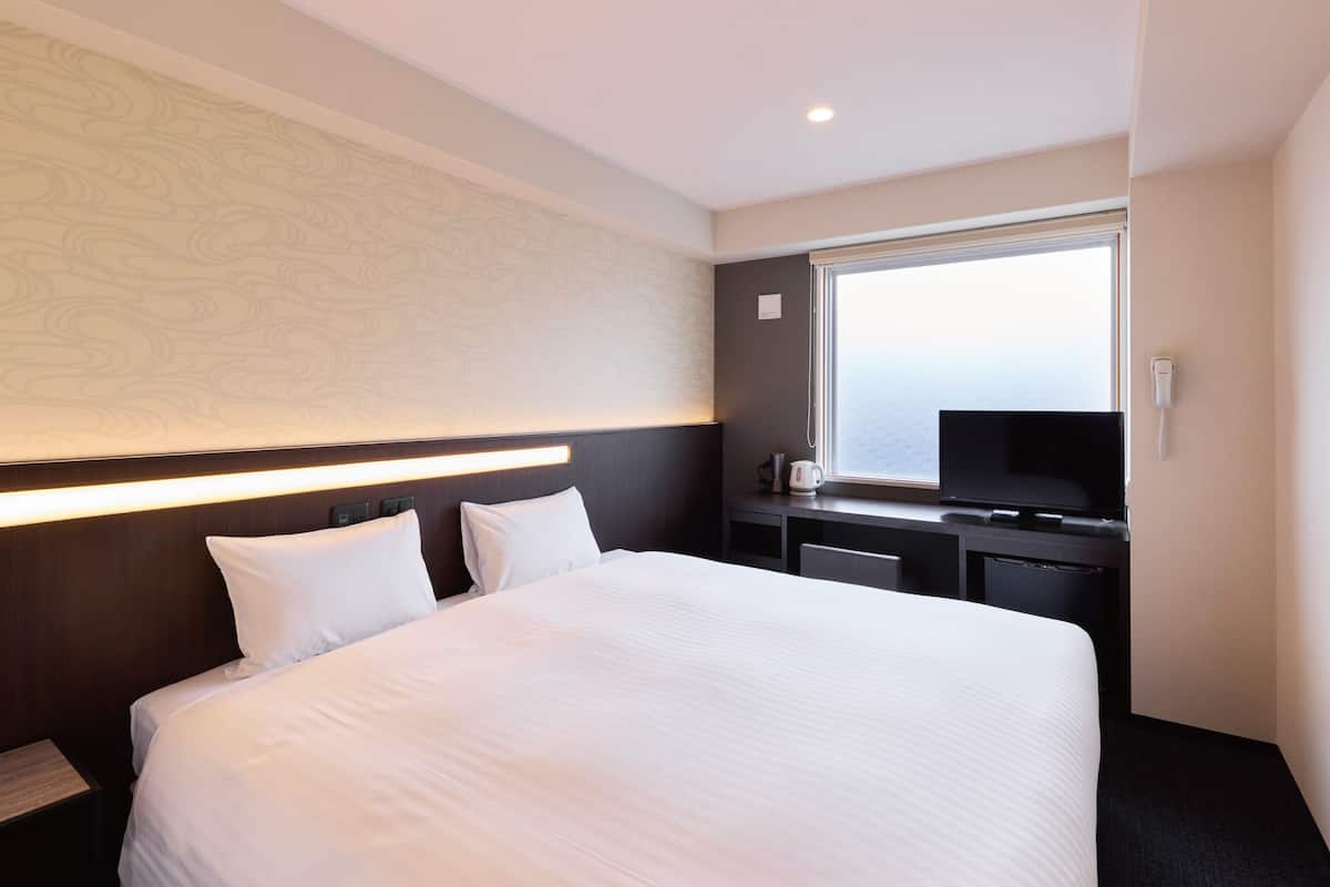 Habitación de hotel con una cama grande, un escritorio con televisor de pantalla plana, una ventana con vistas y un teléfono en la pared.