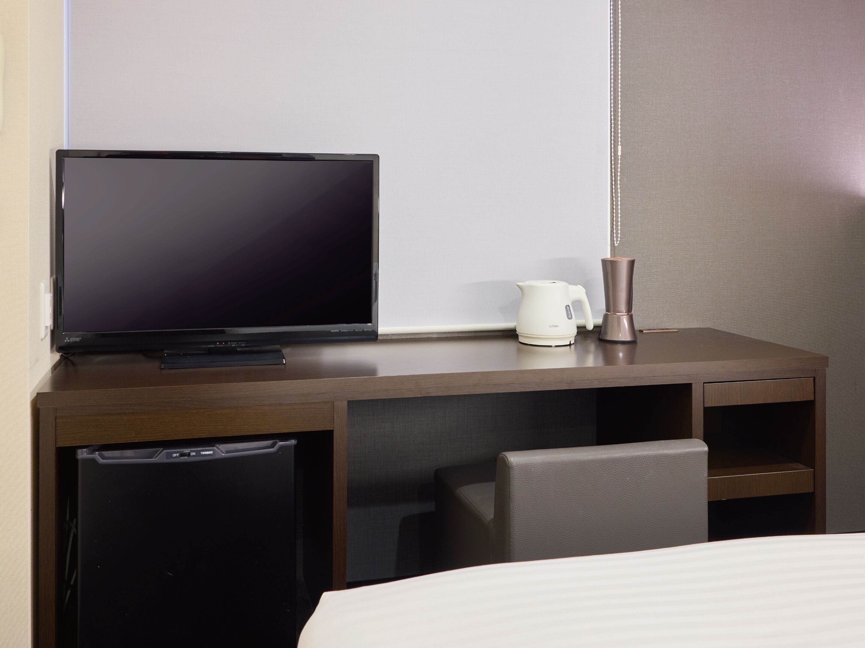 Een hotelkamer met een televisie, koffiezetapparaat, kleine koelkast, stoel en bed.