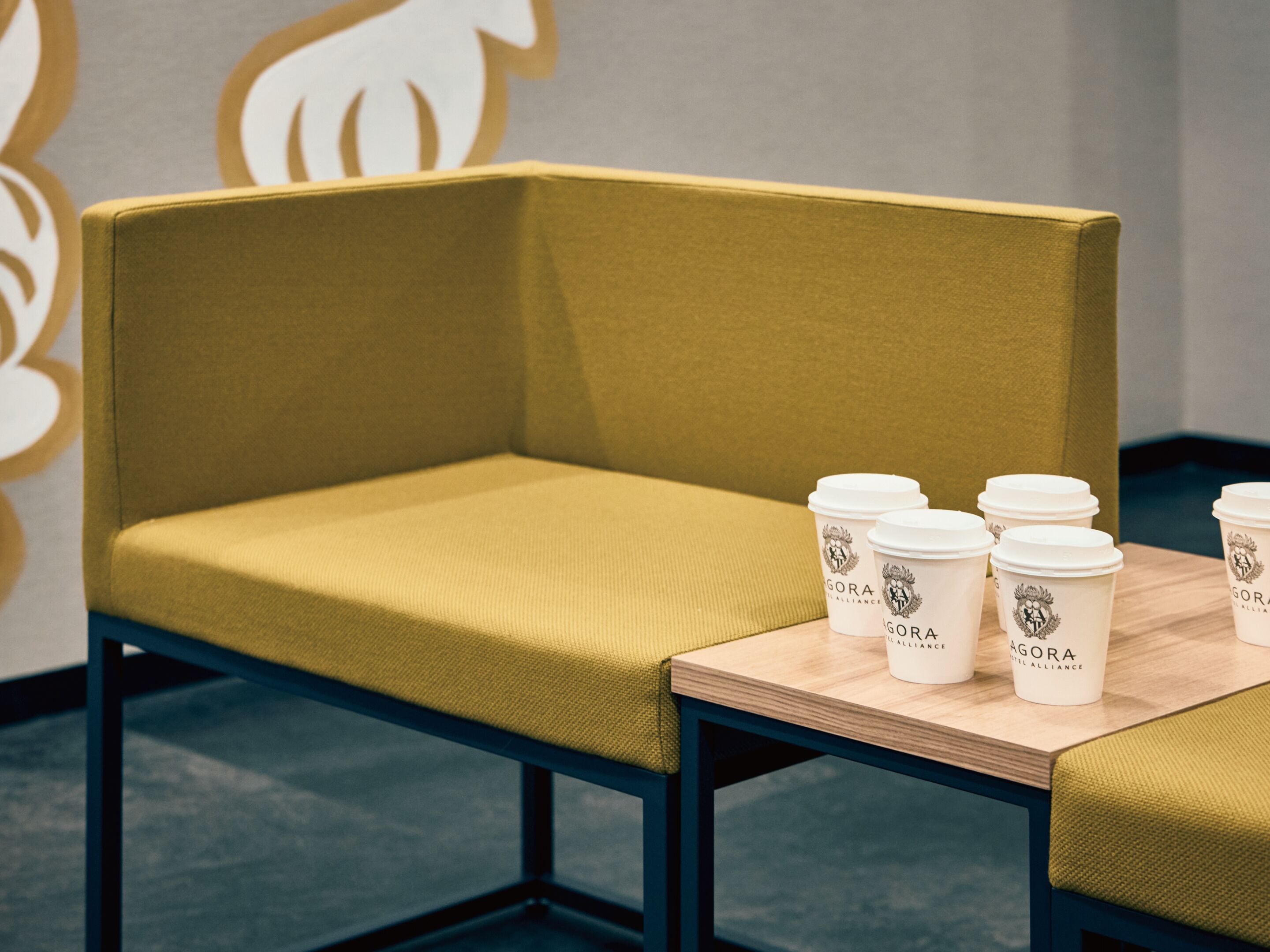 A yellow cushioned chair with a table beside it, holding several white disposable coffee cups with logos.