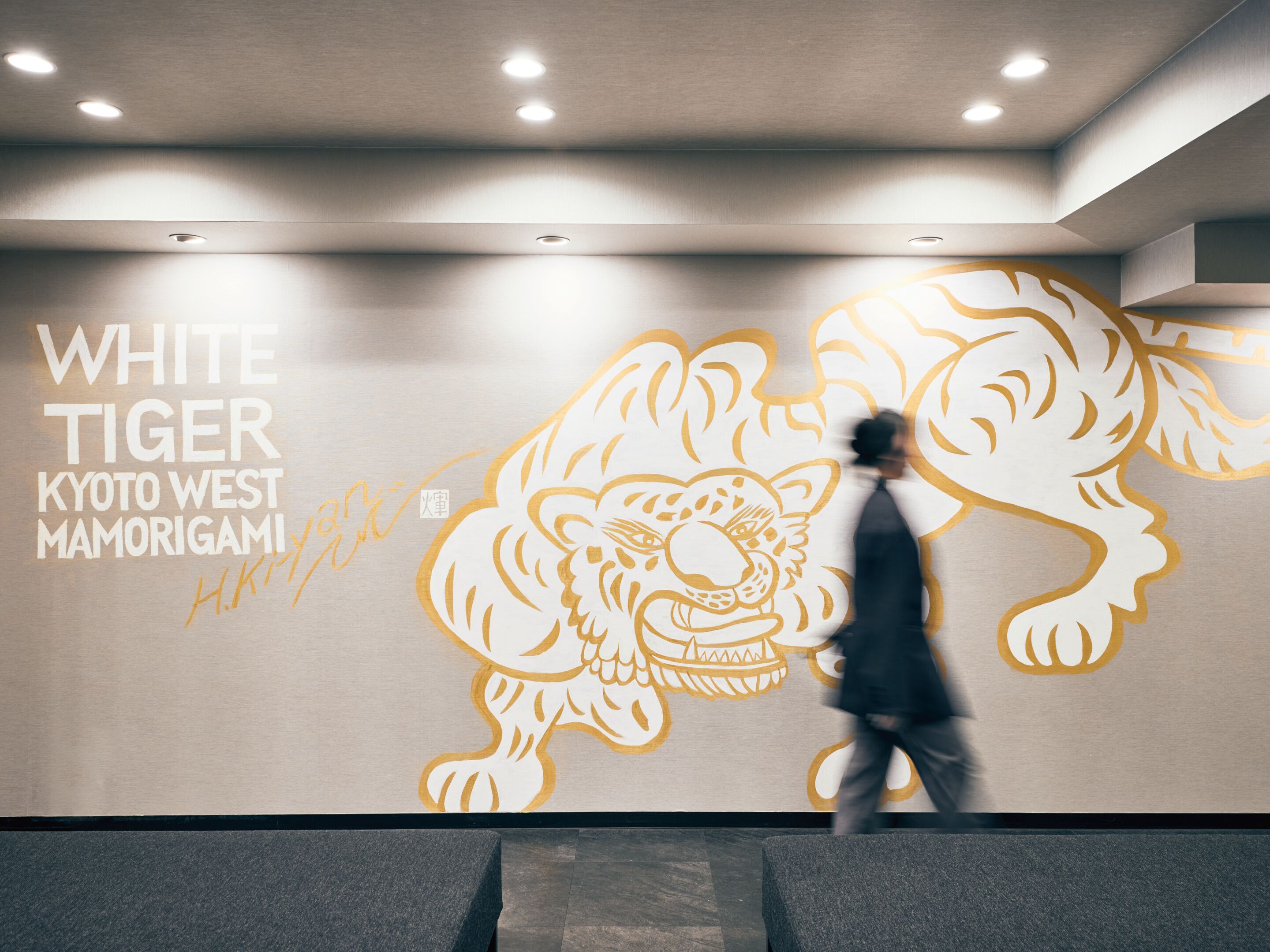 Un mur orné d’une grande fresque représentant un tigre blanc, des spots encastrés au plafond et une personne qui passe.