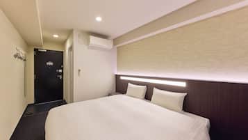 A hotel room with a bed, an air conditioning unit, a door, and a wall-mounted light fixture.