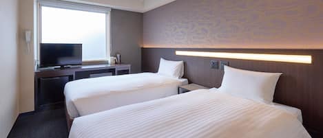 A hotel room with two beds, a desk with a television, and a window.