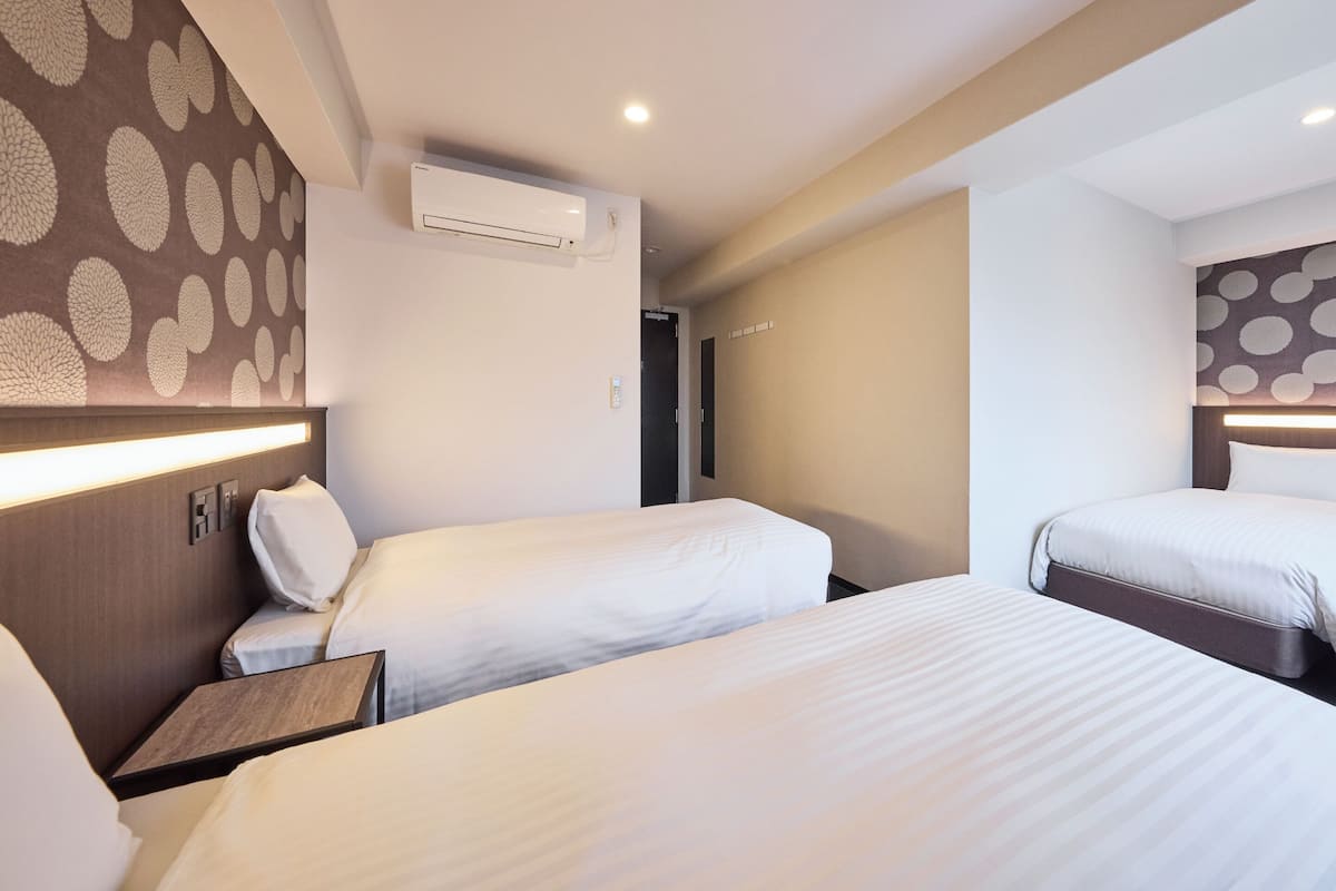 Habitación de hotel con dos camas, aire acondicionado de pared, mesita de noche y cabecero con tira de luz.