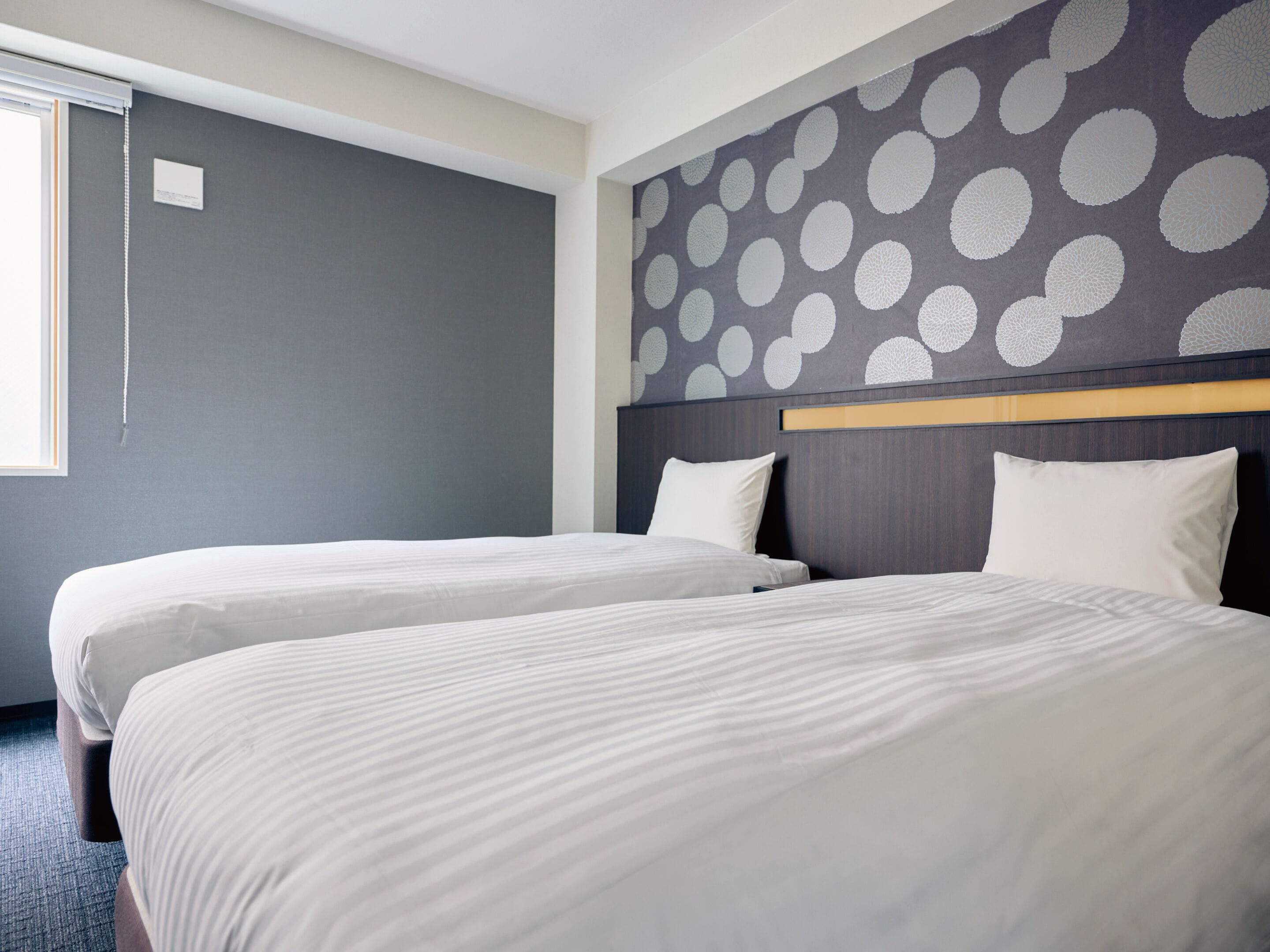 A hotel room with two beds, a grey wall, and a polka dot design on the headboard.