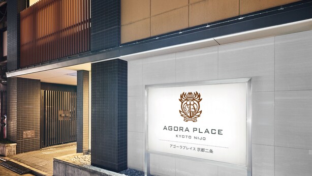 A modern building facade with a prominent entrance, a logo, and the name 'AGORA PLACE' indicating a commercial establishment.