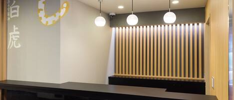 Un espace d’accueil avec un comptoir noir, un mur orné d’un motif circulaire et trois suspensions lumineuses.