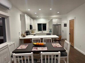 A modern kitchen with white cabinetry, a central island, and a dining area with a black table and white chairs. - The Dam Lakehouse B, Fishing & Boating Basecamp (Grand Coulee)