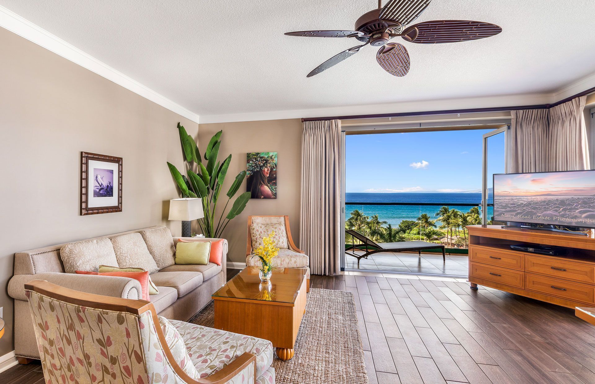 A living room with a sofa, coffee table, TV, and a balcony with a view of the ocean.