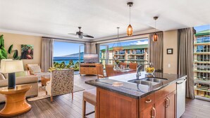 A spacious living area with a large TV, wooden furniture, and a view of the ocean. - Maui Resort Rentals: Honua Kai - 3 Total Bedrooms, Stunning 6th Floor Ocean AND West Maui Mountain Views! (Lahaina)