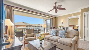 A hotel room with a balcony, a ceiling fan, a sofa, a coffee table, and a dining area with chairs and a table. - Maui Resort Rentals: Honua Kai - 3 Total Bedrooms, Stunning 6th Floor Ocean AND West Maui Mountain Views! (Lahaina)