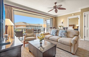 Ein Hotelzimmer mit Balkon, Deckenventilator, Sofa, Couchtisch und Essbereich mit Stühlen und Tisch.