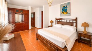 Une chambre à coucher avec un lit en bois, une table de chevet, une lampe, un tableau accroché au mur et une porte donnant sur une autre pièce.