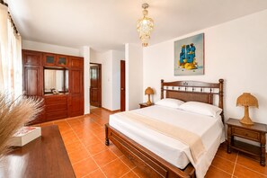 Een slaapkamer met een houten bed, een nachtkastje, een lamp, een schilderij aan de muur en een deur naar een andere kamer.