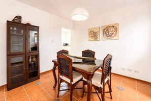 Un coin repas comprenant une table à plateau en verre, quatre chaises en bois, un meuble avec des portes en verre et deux œuvres d’art accrochées au mur.