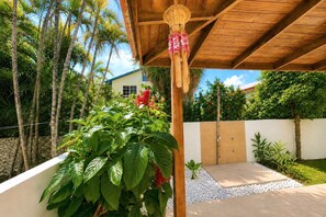 Un espace extérieur abrité, doté d’un plafond en bois, d’un mur blanc et d’un petit jardin agrémenté de galets et de plantes.