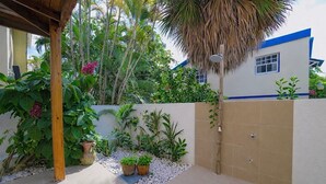 Um espaço coberto ao ar livre com piso de concreto, ladeado por um muro baixo com plantas em vasos e uma palmeira.
