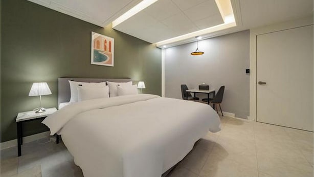 A hotel room with a large bed, bedside tables, a desk with a chair, and a door. - Page 9 Hotel (Seoul)