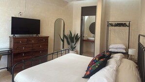 A bedroom with a bed, a dresser, a television, a ceiling fan, a mirror, a plant, and a clothing rack. - Casa Bélanger (Mérida)