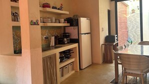 A compact kitchen with a refrigerator, stove, and shelves. There is a dining table with chairs and a window with a view of the outside. - Casa Bélanger (Mérida)