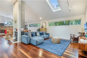A spacious living area with a large sectional sofa, a wooden dining table, and a kitchen in the background. - Our Happy Place, Byron Bay - Pool & Hot Tub (Byron Bay)