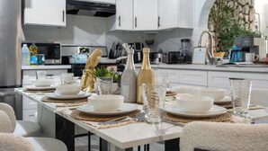 Une cuisine moderne avec des meubles blancs, un plan de travail en marbre et un coin repas aménagé pour six personnes, avec des assiettes, des bols et des verres blancs.