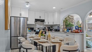 Une cuisine moderne avec des meubles blancs, des appareils en acier inoxydable et un coin repas avec une table dressée pour quatre personnes.