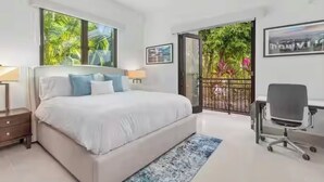 Quarto moderno com cama grande, escrivaninha e varanda com vista para o verde.