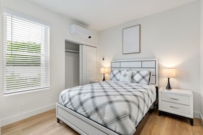Een slaapkamer met een bed, nachtkastjes, een kledingkast en een raam met jaloezieën.
