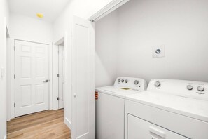 Een wasserij met twee witte Whirlpool wasmachines en drogers, houten vloeren en witte muren.