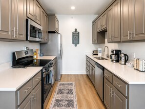 A modern kitchen with stainless steel appliances, wooden cabinets, a central island, and a welcome sign. - Modern New‑Build Suite • Hot Spring• Downtown (Hot Springs)