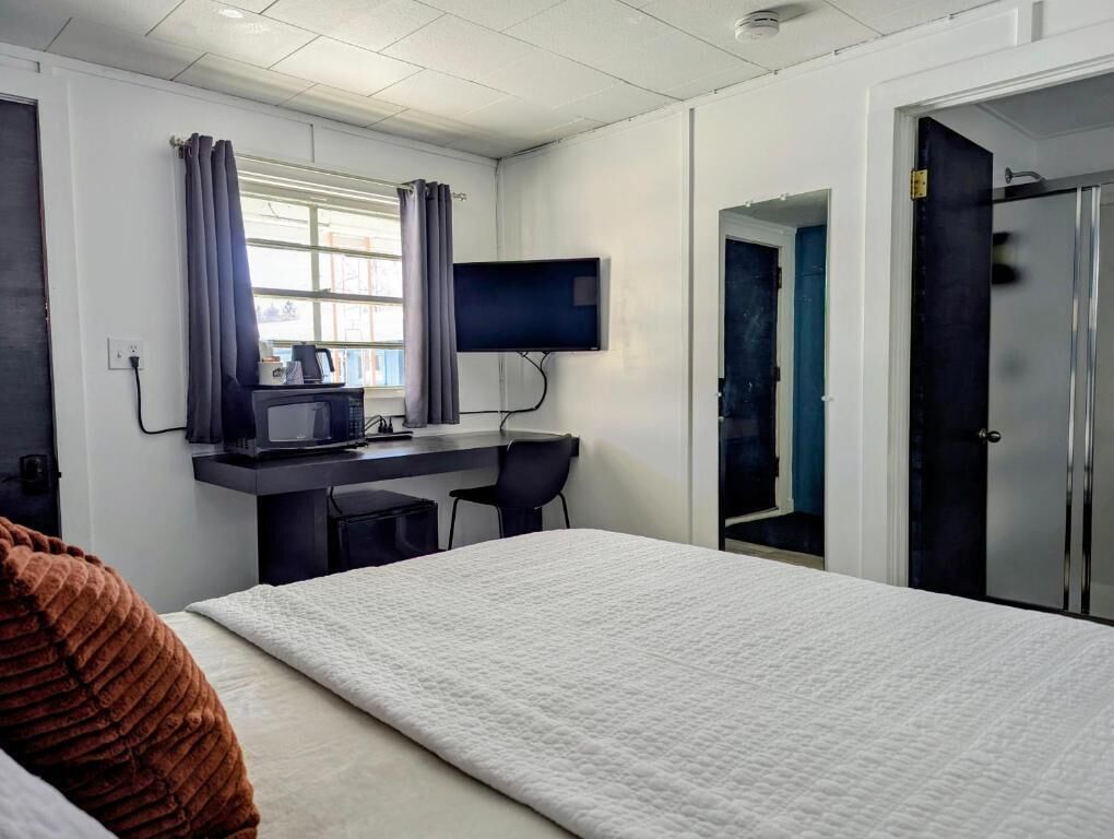 A hotel room with a bed, a desk with a computer, a TV, and a door.