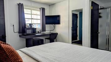 A hotel room with a bed, a desk with a computer, a TV, and a door.