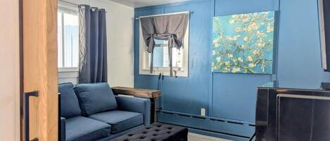 A modern living room with a blue wall, a sofa, an ottoman, a TV, and a painting.