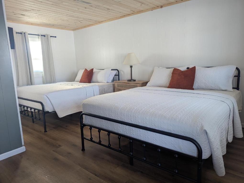 Een kamer met twee bedden, een nachtkastje, een lamp en een raam met gordijnen.