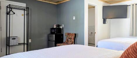 A room with two beds, a TV mounted on the wall, a wooden ceiling, and a door leading to another room.