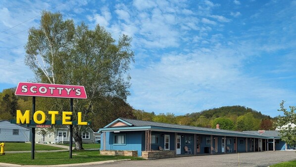 Ein Motel mit blauer Fassade, einer Veranda mit Stühlen und einem Schild, das freie Zimmer anzeigt.