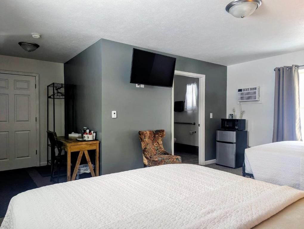 Une chambre d’hôtel comprenant un lit, un bureau, une chaise, une télévision, un coin cuisine et une porte donnant sur une autre pièce.