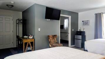 Une chambre d’hôtel comprenant un lit, un bureau, une chaise, une télévision, un coin cuisine et une porte donnant sur une autre pièce.