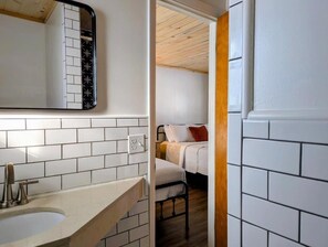 Ein Badezimmer mit weißen Fliesen, einem Waschbecken und einem Spiegel.