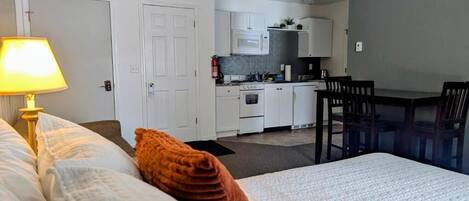 Una habitación de hotel con cama, escritorio, silla, lámpara y kitchenette.